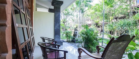 A covered patio with wooden furniture and a view of a lush garden.