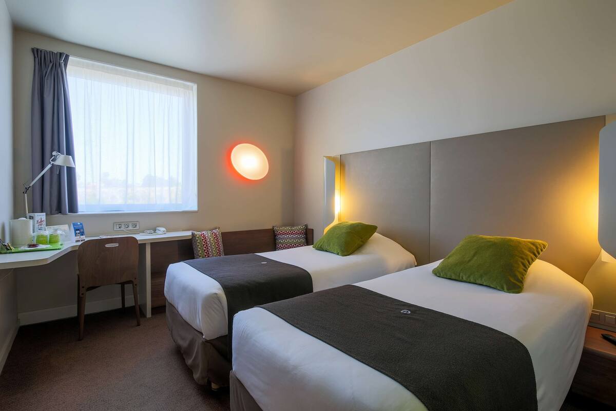 Een hotelkamer met twee bedden, een bureau, een stoel en een raam met gordijnen.