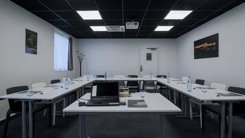 Un salón de conferencias con una larga mesa, sillas, computadoras portátiles, botellas de agua y un proyector.
