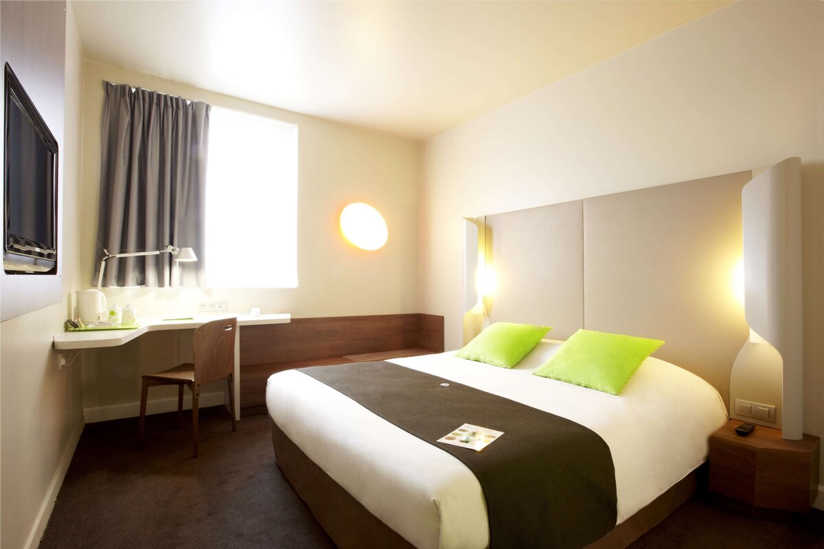 Een hotelkamer met een bed, bureau, stoel en een raam met gordijnen.