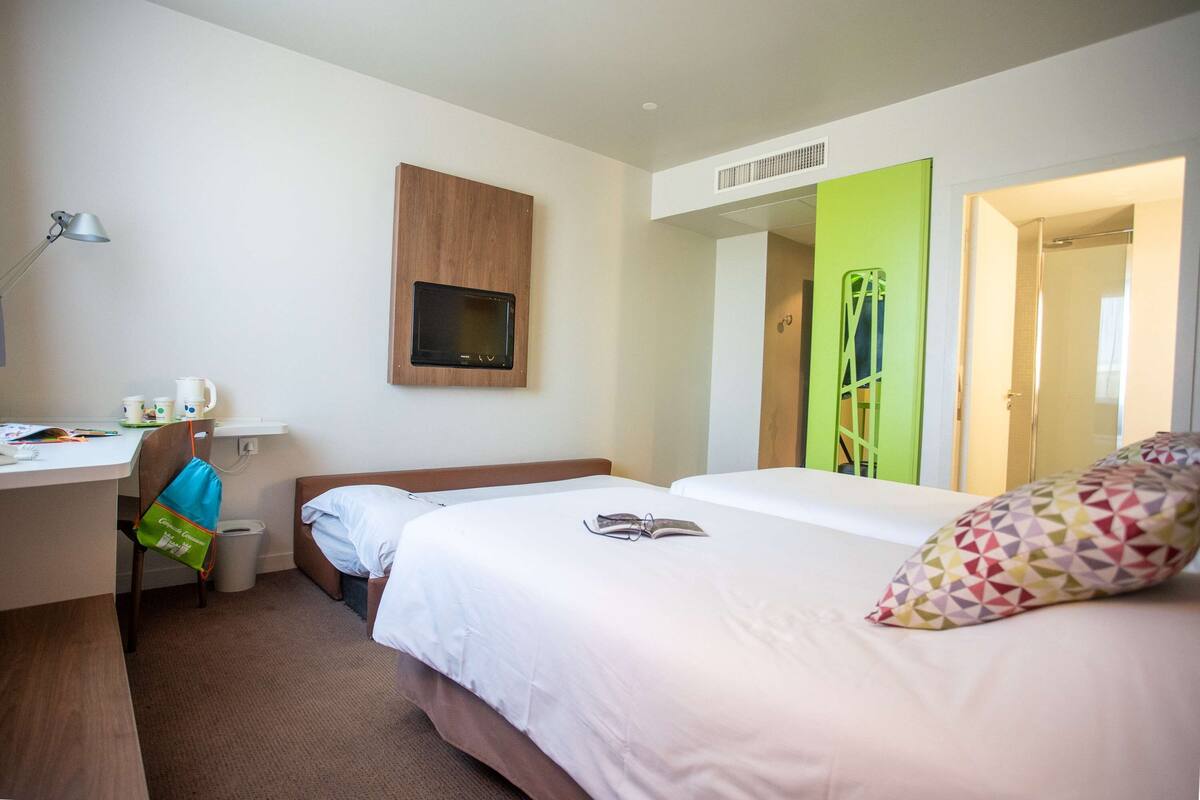 Een hotelkamer met een bed, bureau, stoel, televisie en deur naar de badkamer.