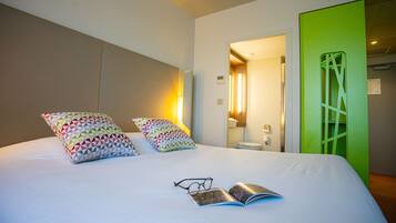 A hotel room with a bed, pillows, a book, and glasses.