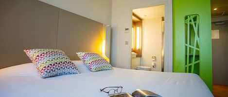 A hotel room with a bed, pillows, a book, and glasses.