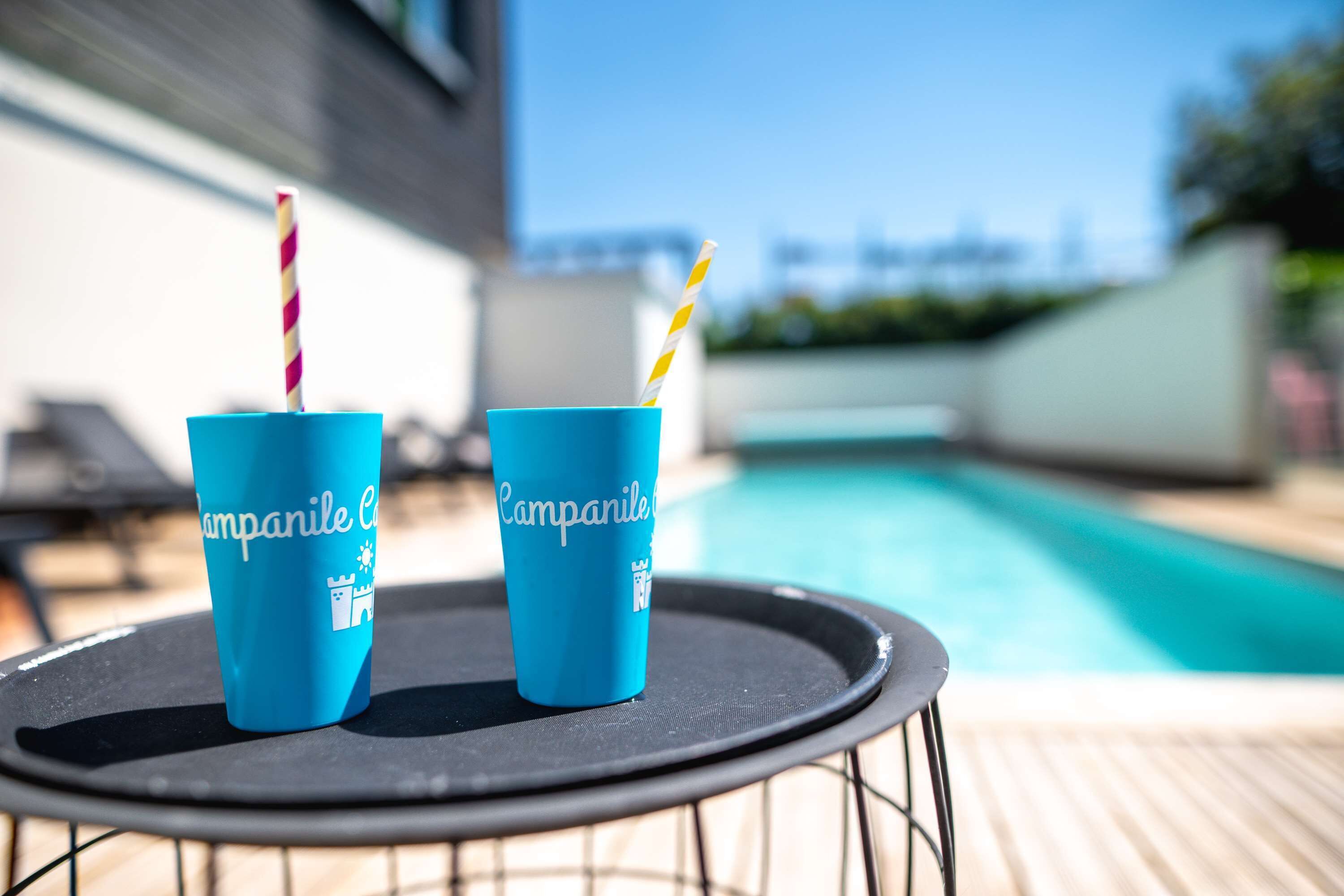Two blue cups with 'Campanile' branding on a table by a pool.