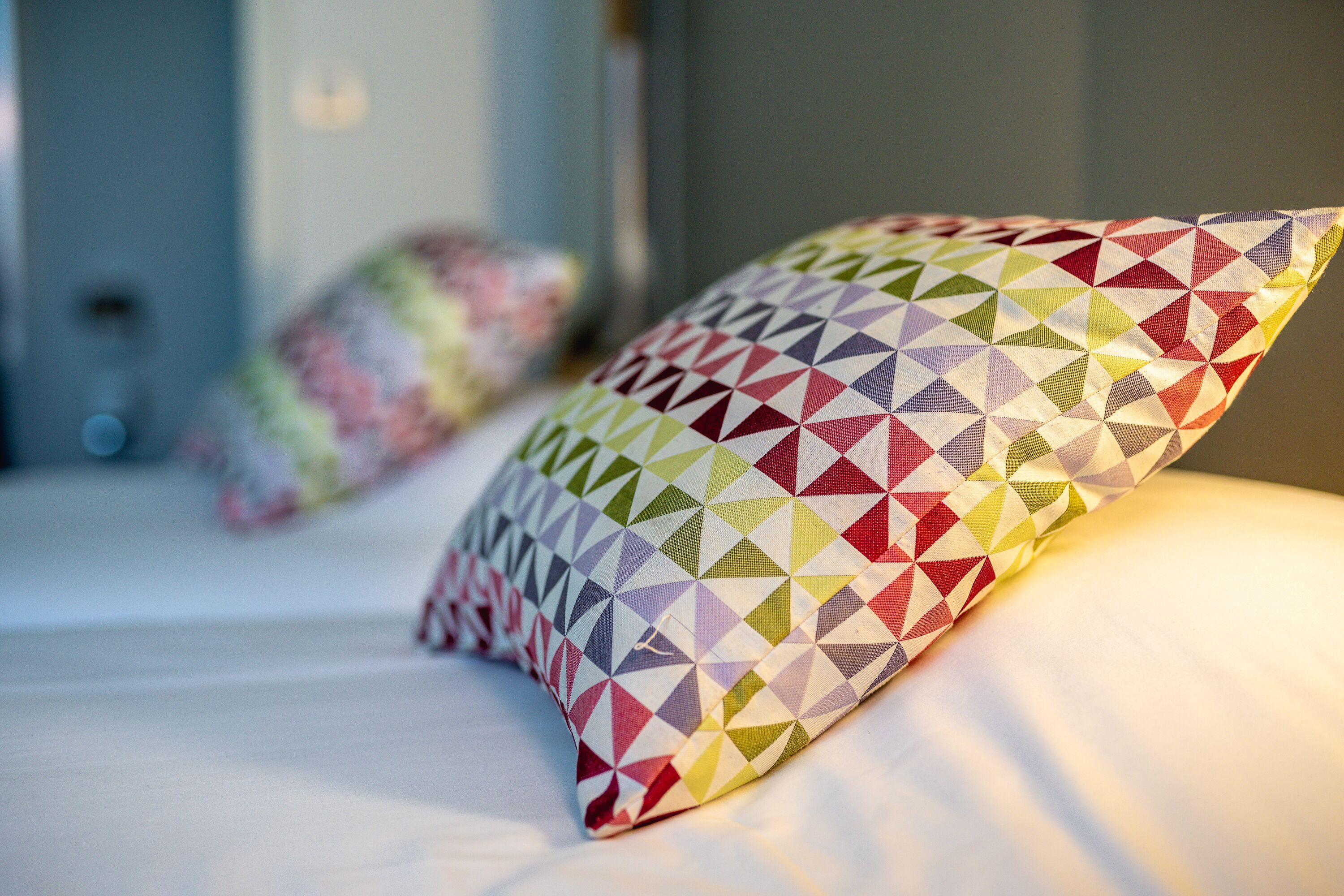 Una cama con dos almohadas, una con un estampado geométrico colorido y otra con diseño floral.