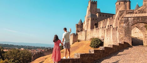 Un castillo de piedra histórico con almenas y torres, un camino de adoquines y un cielo azul despejado.