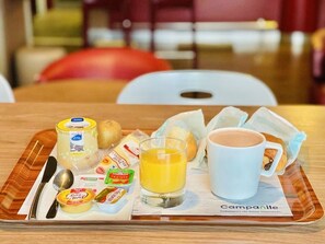 Bandeja de desayuno con una taza de café, vaso de jugo de naranja, queso, mantequilla, pan y un periódico.