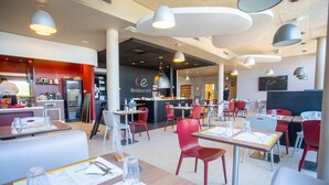 Un intérieur de restaurant moderne avec des sièges rouges et blancs, un bar central et un éclairage suspendu au plafond.