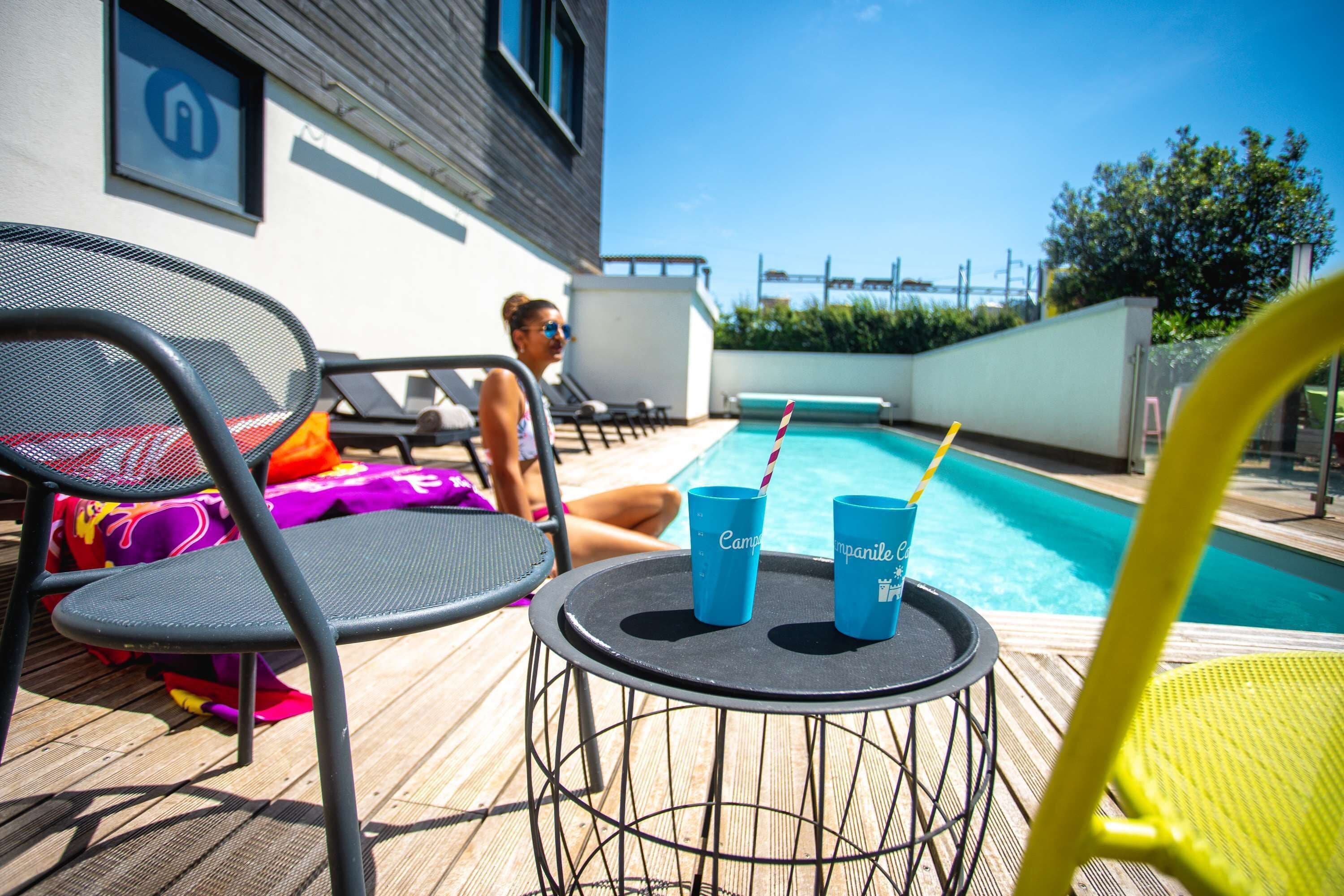 Un espace aménagé au bord de la piscine, avec des chaises longues, une table sur laquelle sont posées deux tasses et la piscine elle-même.