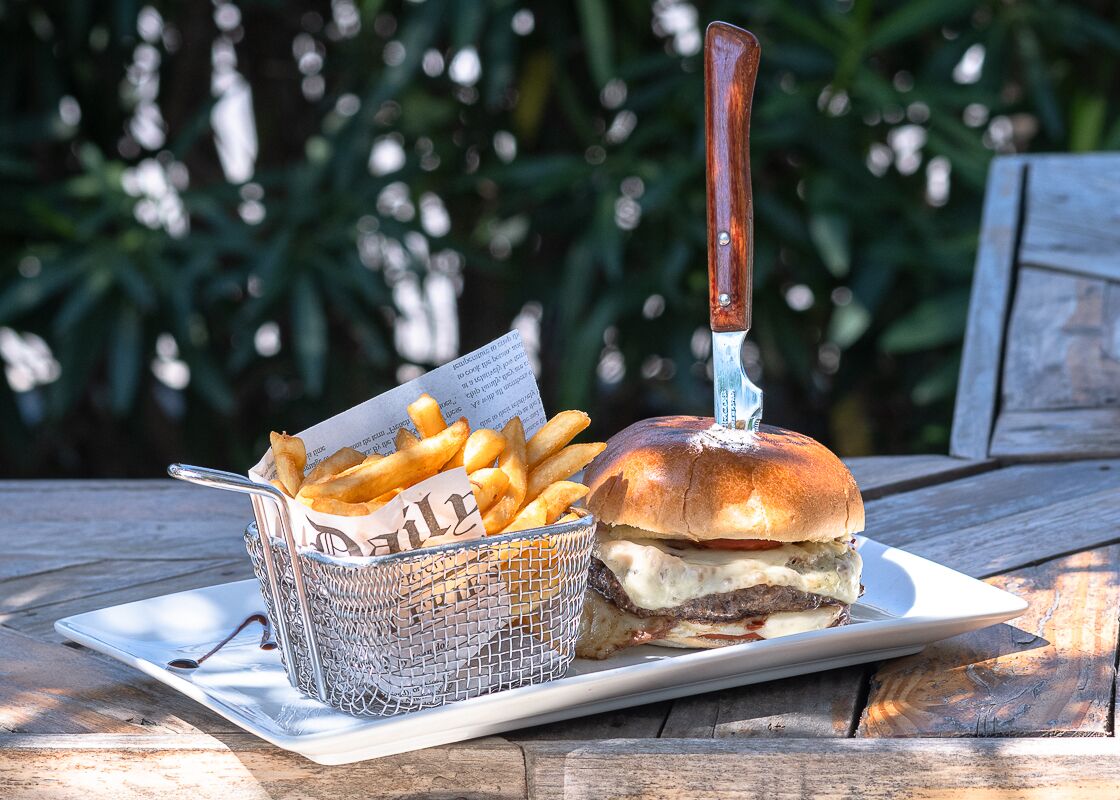Un hamburger avec un couteau sur une assiette, un panier de frites et un menu sur une table en bois.