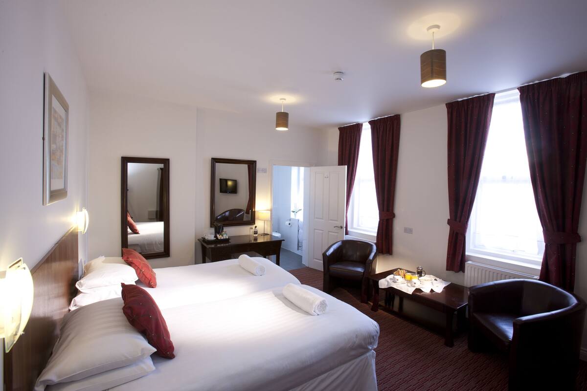 A hotel room with a large bed, a desk, a chair, and a window with curtains.