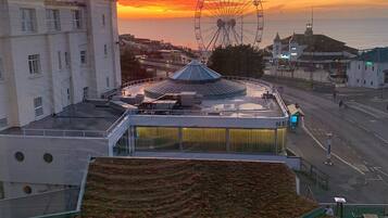A modern building with a rooftop garden, a Ferris wheel in the background, and a sunset sky.
