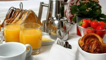 A breakfast setup with a croissant, orange juice, coffee cups, a teapot, and strawberries.