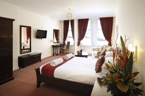 A hotel room with a large bed, a desk, a chair, a TV, and a window with curtains. - Sea Stone Hotel (Bournemouth)
