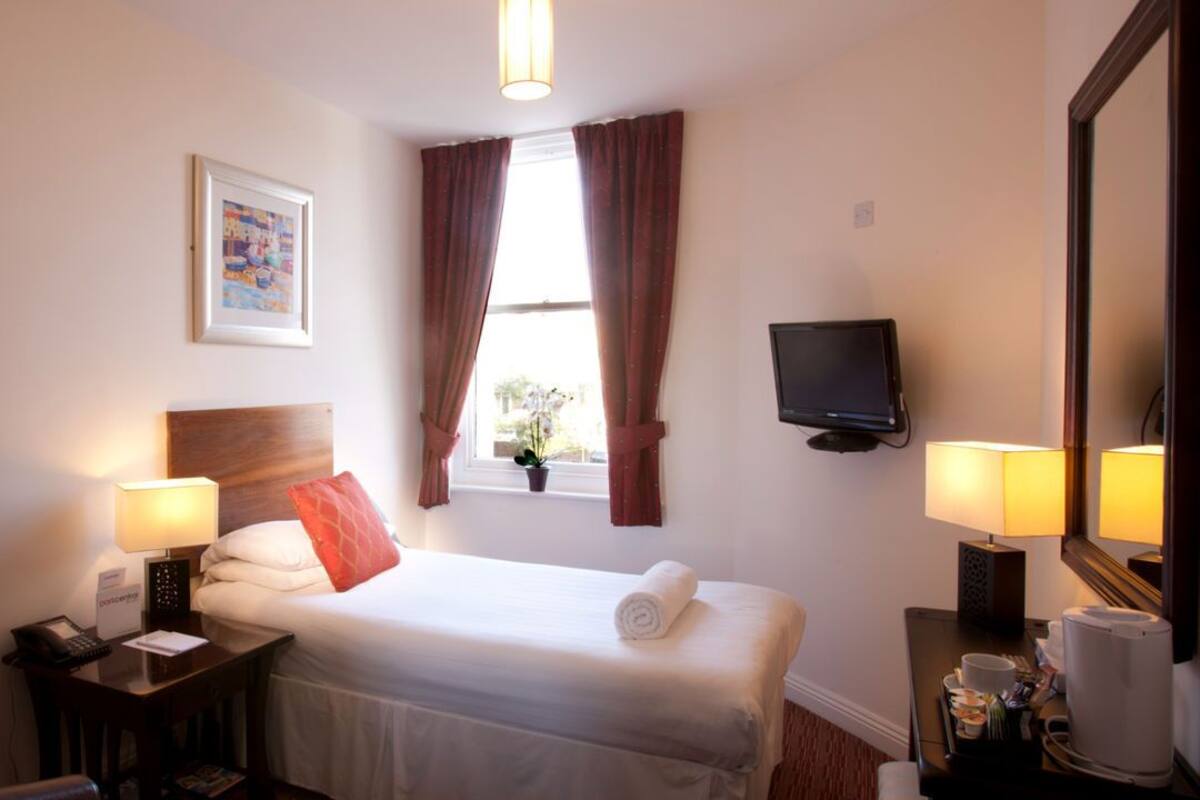 A hotel room with a bed, bedside lamps, a television, a desk with a telephone, and a window with curtains.