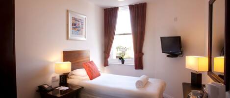 A hotel room with a bed, bedside lamps, a television, a desk with a telephone, and a window with curtains.