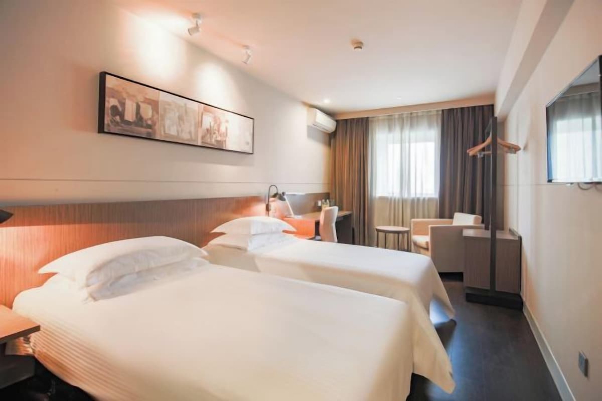 A hotel room with two beds, a desk, a chair, and a large window with curtains.