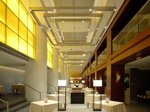 Un hall d’hôtel avec un long couloir, des tables, des chaises et un comptoir d’accueil.