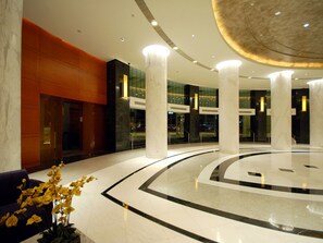 Un hall d’entrée spacieux, doté d’un sol en marbre, de grandes colonnes et d’un éclairage moderne.
