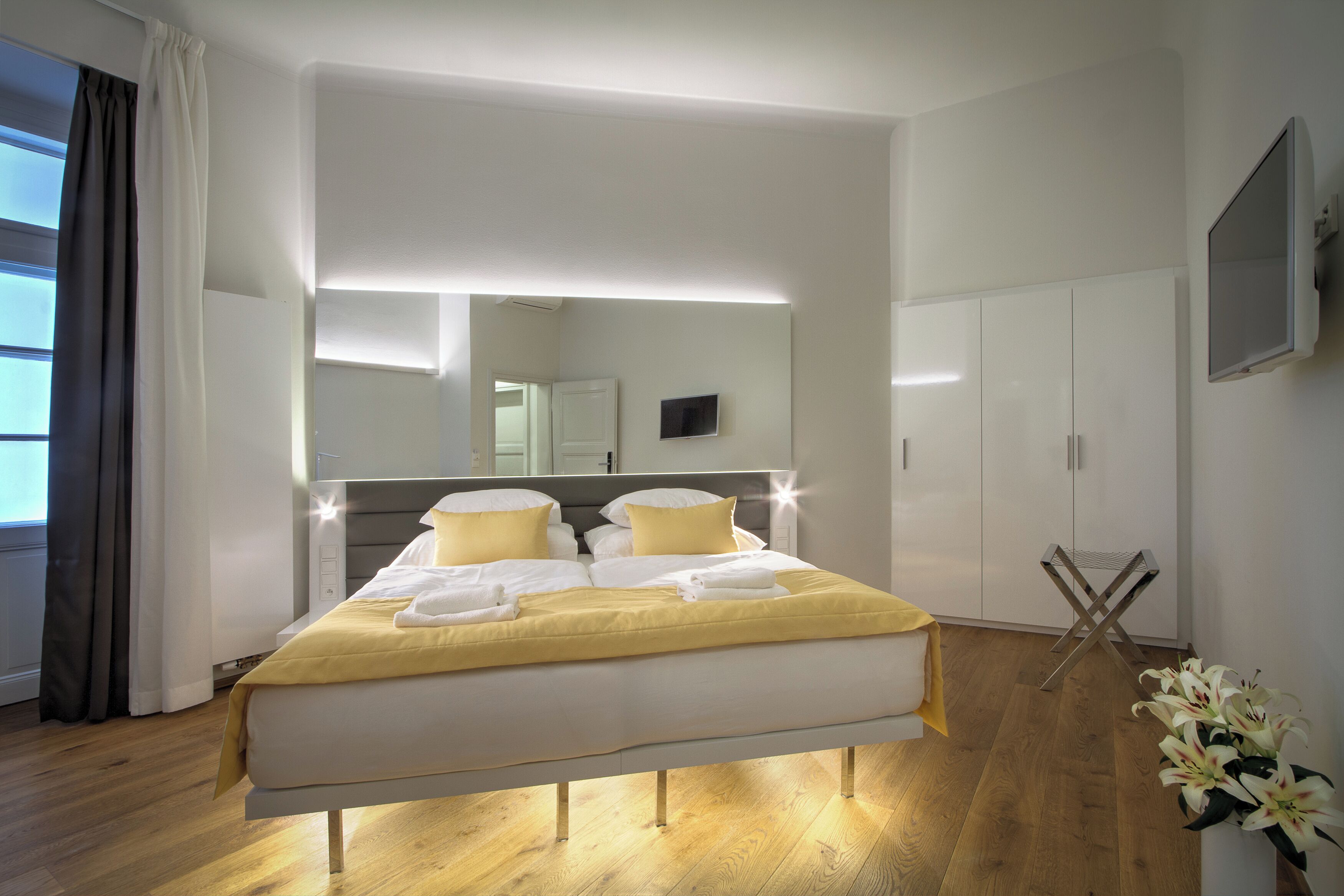 A modern hotel room with a large bed, a flat-screen TV, a wardrobe, and a mirror.