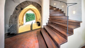 Una escalera de madera con barandilla metálica que conduce a un nivel superior con un arco de piedra y una pared verde.