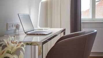 A modern room with a laptop on a desk, a chair, a TV on the wall, and a window with curtains.