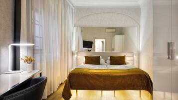 A modern hotel room with a large bed, a desk with a chair, a TV, and a mirror.