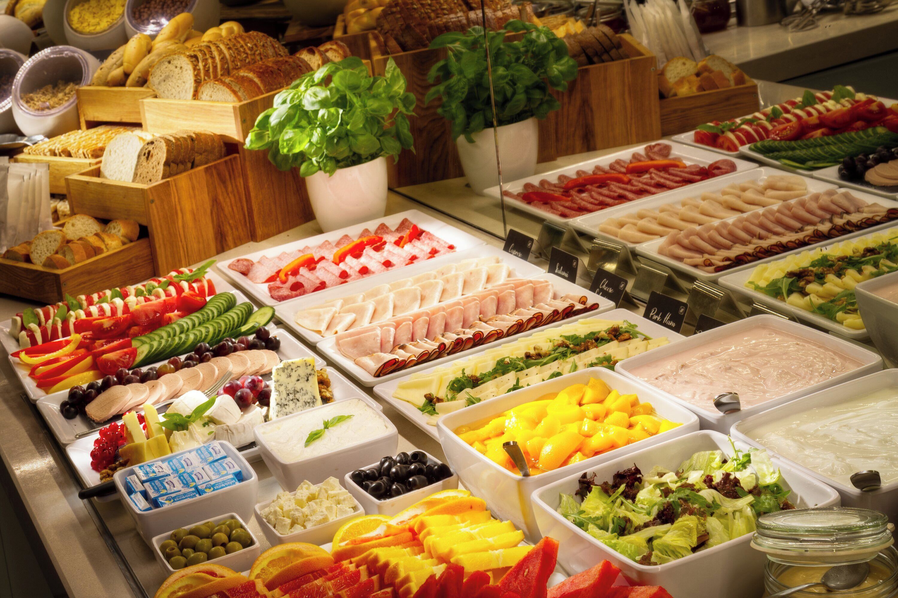 A buffet with various food items including meats, cheeses, fruits, and salads.