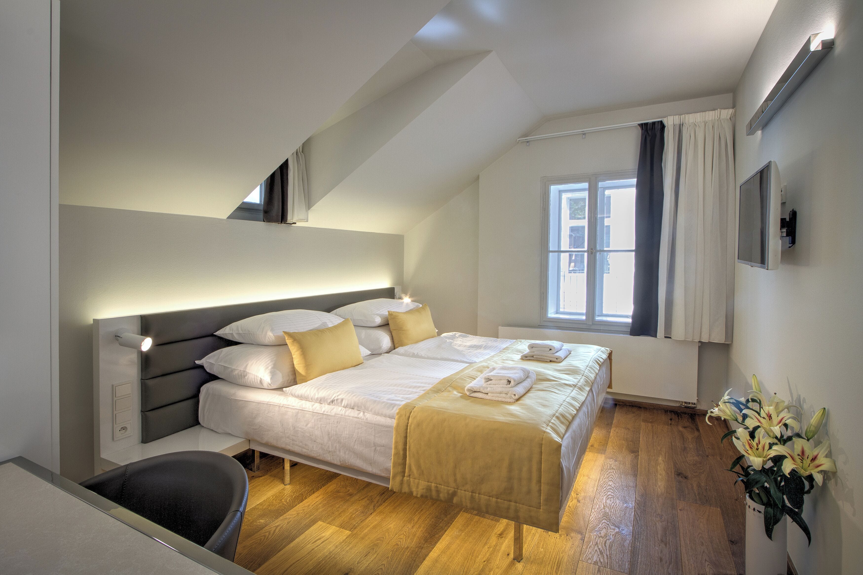 Un dormitorio moderno con cama, mesita de noche y ventana con cortinas.
