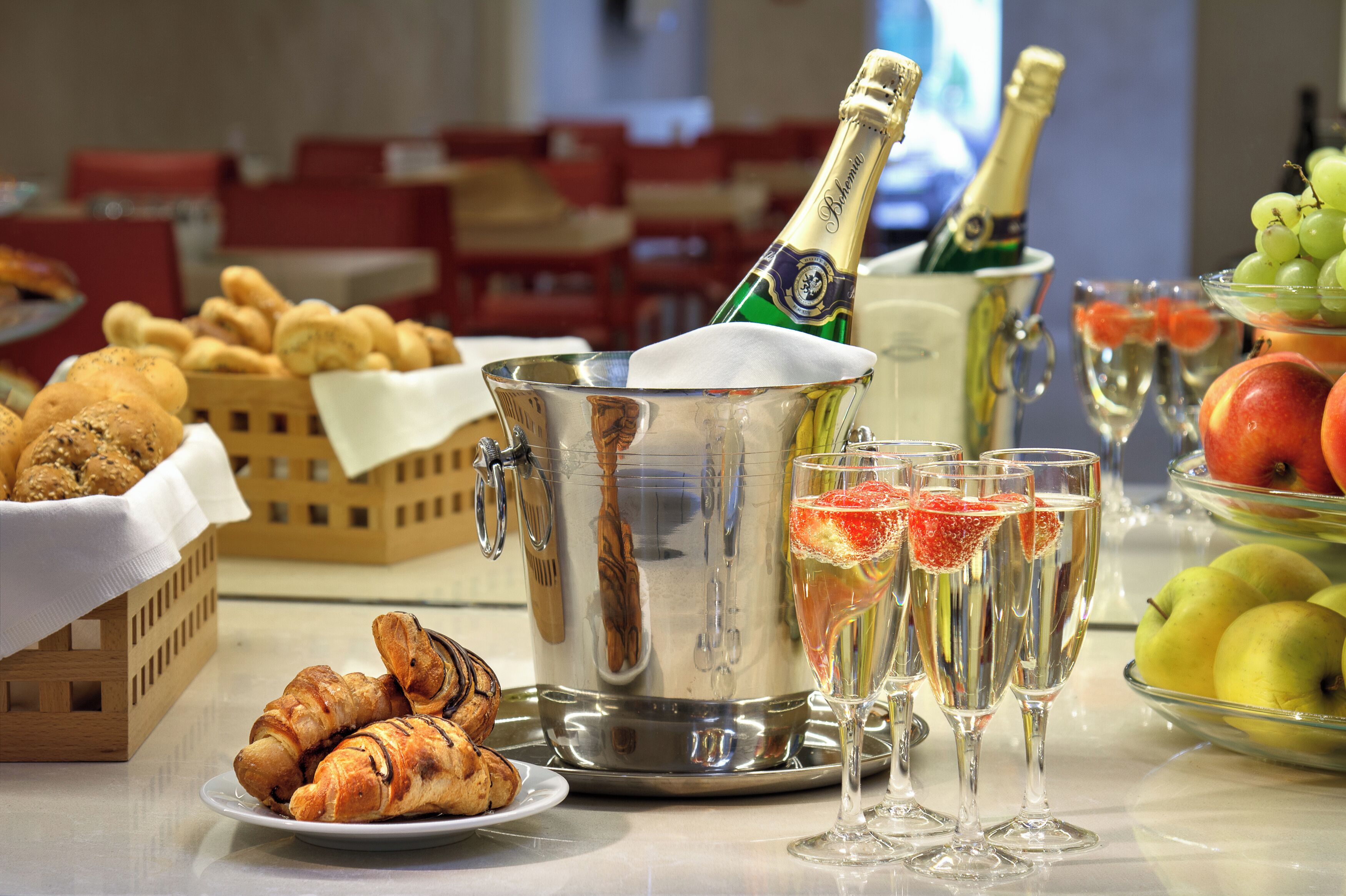 Un bufé de desayuno con croissants, una botella de champán y fruta.