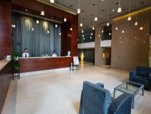 A modern hotel lobby with a reception desk, seating area, and a large window.