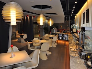 Interior de restaurant modern amb taules rodones, cadires blanques i llums penjants.