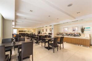 A modern hotel dining area with multiple tables and chairs, a counter with a cash register, and framed artwork on the walls.