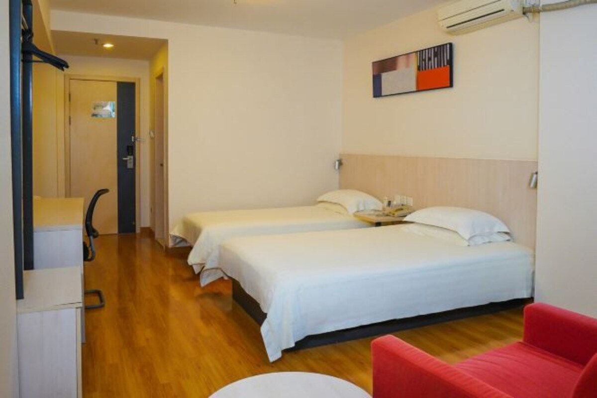 A hotel room with two beds, a red chair, a desk, and a painting on the wall.
