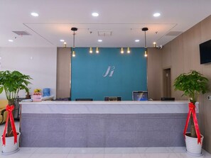 A reception desk with a teal-colored backdrop, a flat-screen TV, and a digital display. There are two potted plants with red ribbons on either side of the desk.