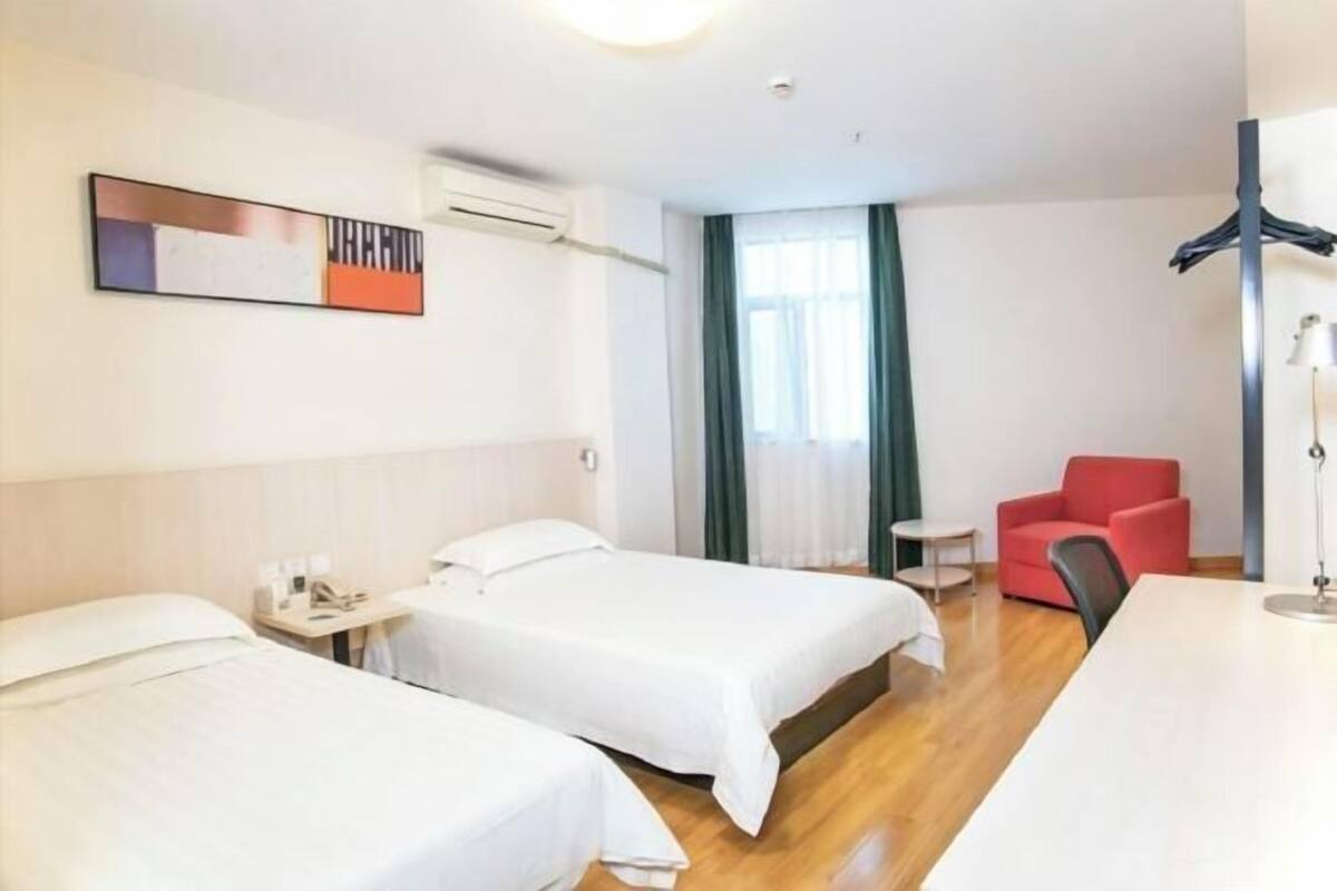 Une chambre d’hôtel avec deux lits, une chaise rouge, un bureau et une lampe.
