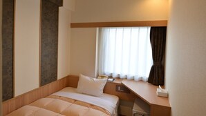 Ett hotellrum med en säng, ett skrivbord, en telefon och ett fönster med gardiner.