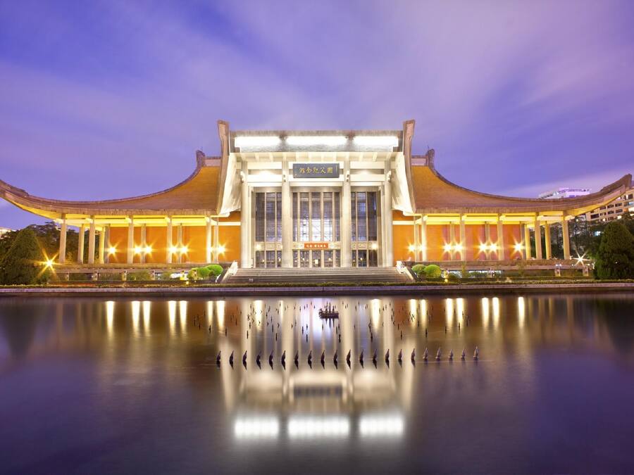 A traditional building with a symmetrical facade and a reflection in the water in front.