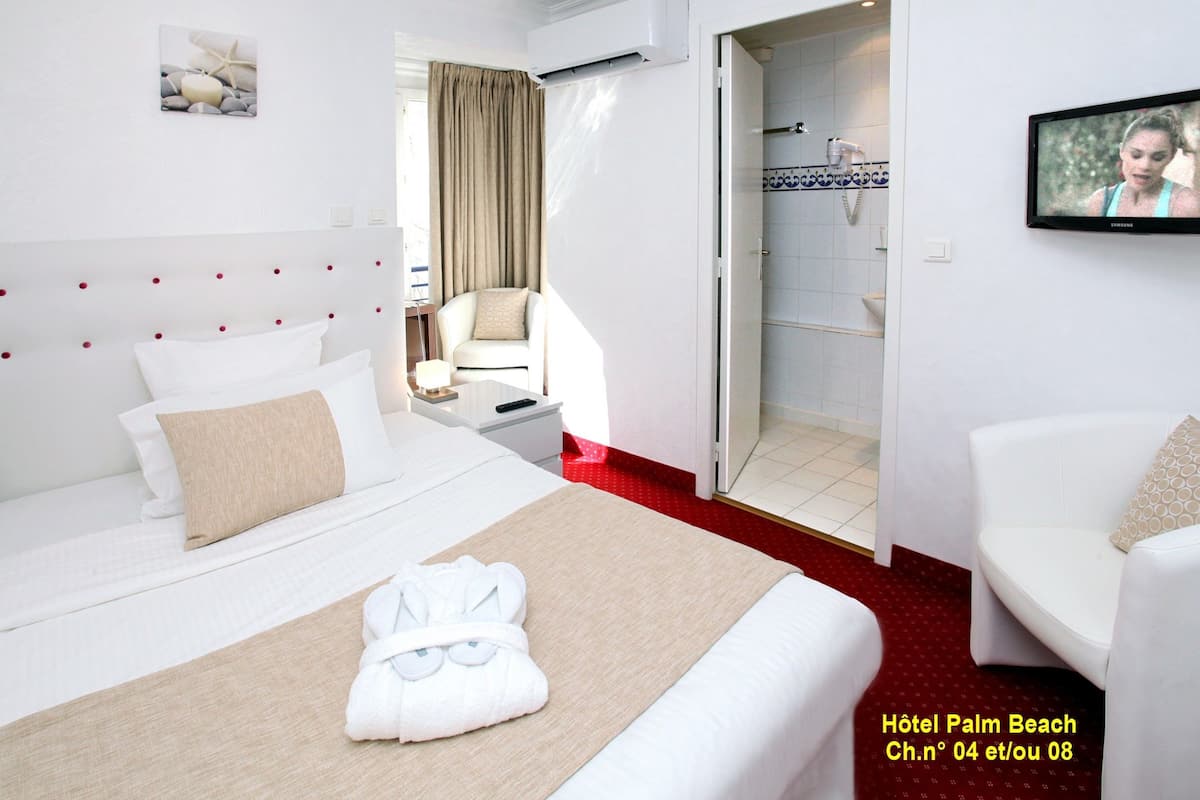 A hotel room with a bed, a chair, a TV, and a bathroom visible through an open door.