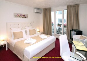 Habitación de hotel con una cama grande, un escritorio con silla, televisión y balcón con mobiliario exterior.