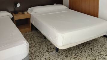 Une chambre d’hôtel avec deux lits simples, une table de chevet en bois avec une lampe, un tableau encadré au mur et une armoire en bois.