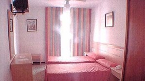 Une petite chambre d’hôtel composée d’une seule pièce, avec deux lits, un bureau et une chaise.