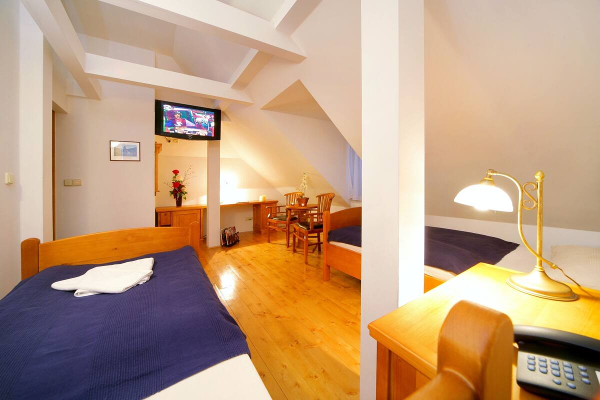 Ein Zimmer mit zwei Betten, einem Fernseher, einem Schreibtisch mit Lampe und einem Sessel.