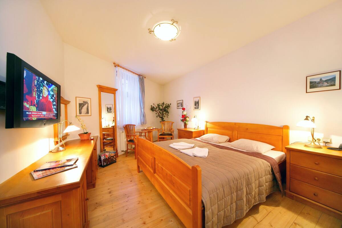 Ein Schlafzimmer mit einem hölzernen Bett, einem Schreibtisch mit Lampe, einem Fernseher und einem Sessel.