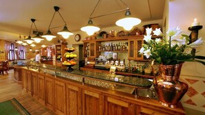 Een bar met houten kasten, een marmeren aanrechtblad, hangende pendantlampen en een koperen vaas met bloemen.
