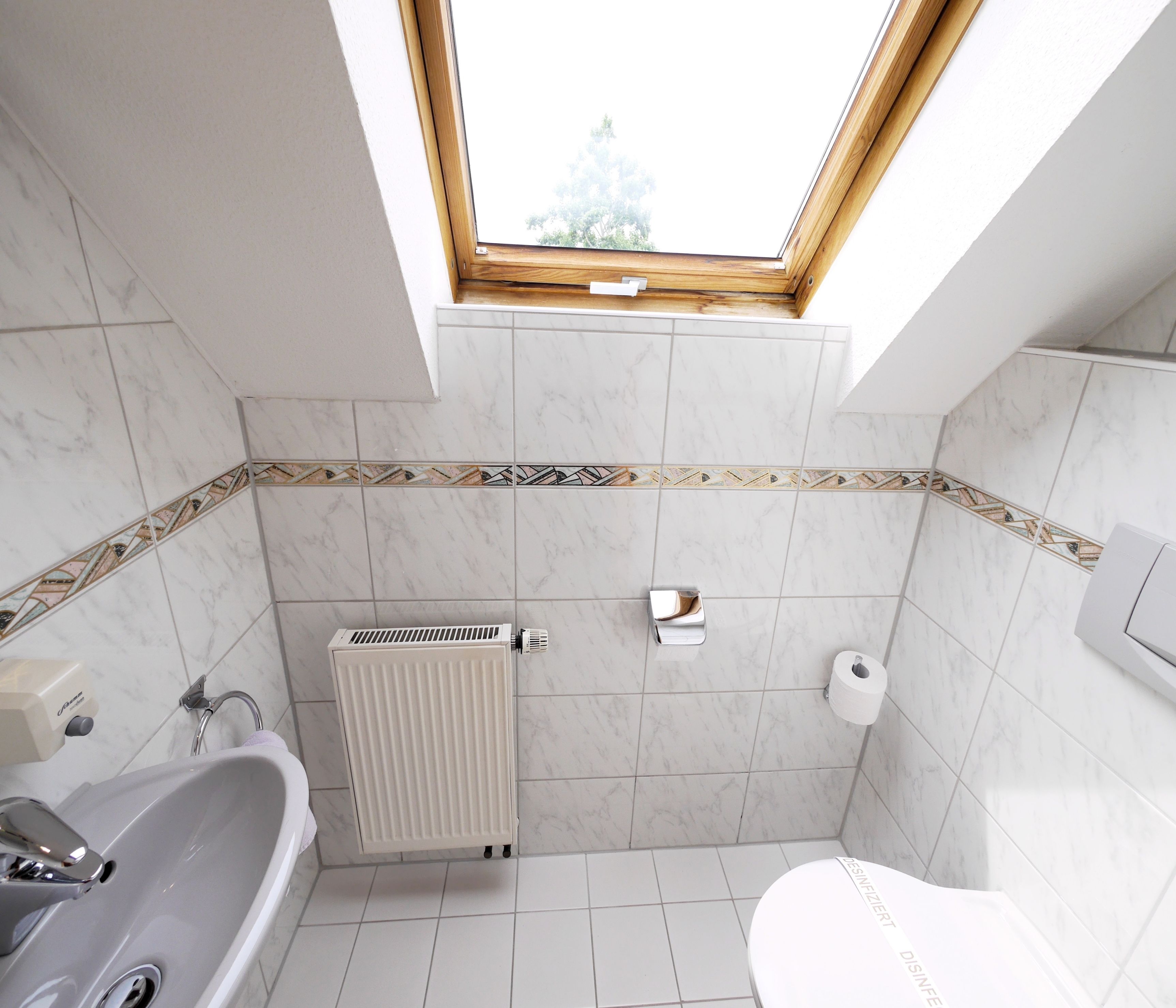 A bathroom with a skylight, a bathtub, a toilet, and a radiator.