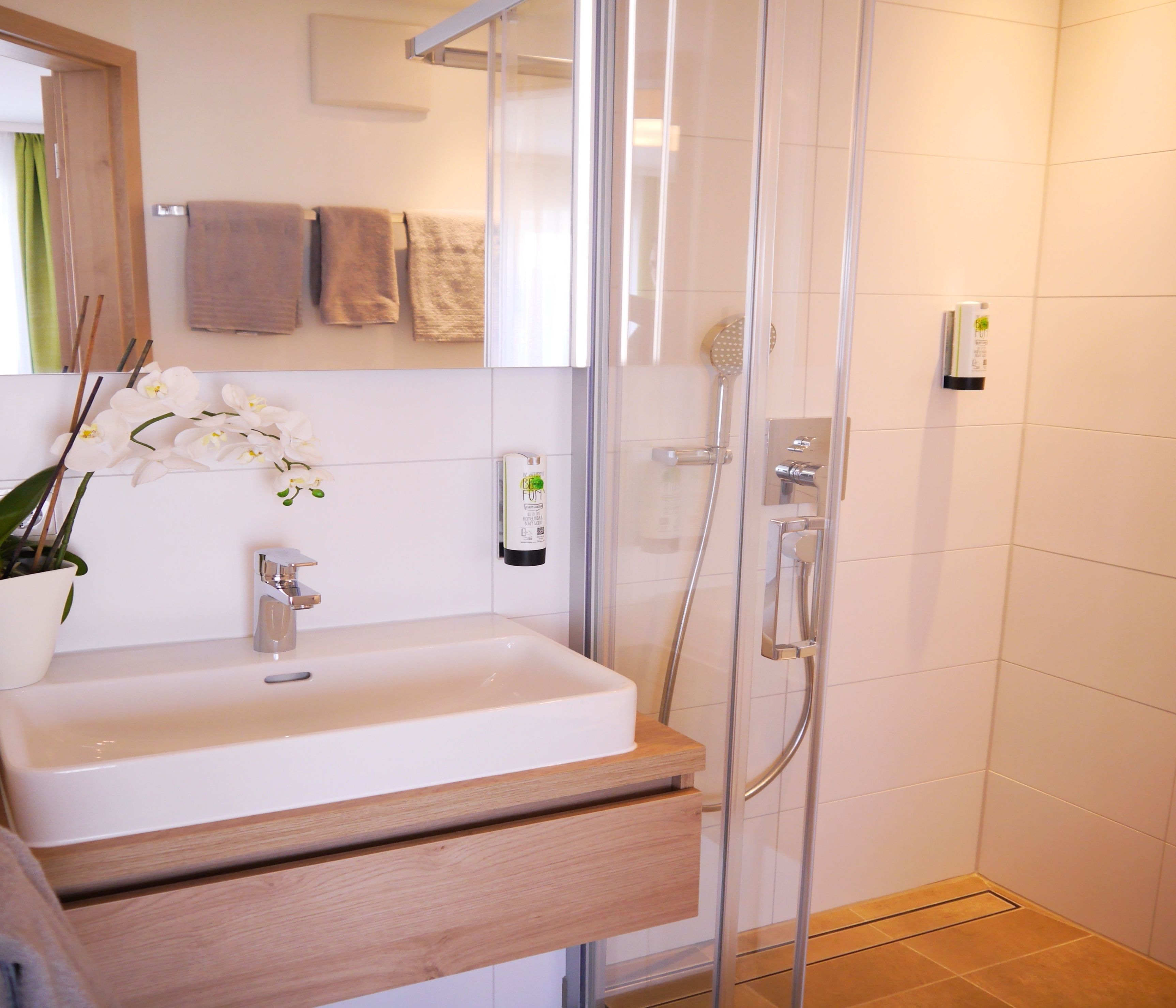 A modern bathroom with a white sink, a glass shower enclosure, and a wooden vanity.