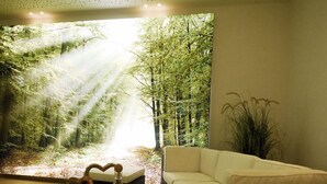 Un salon avec une grande fenêtre, un canapé blanc, une table basse foncée et une plante.
