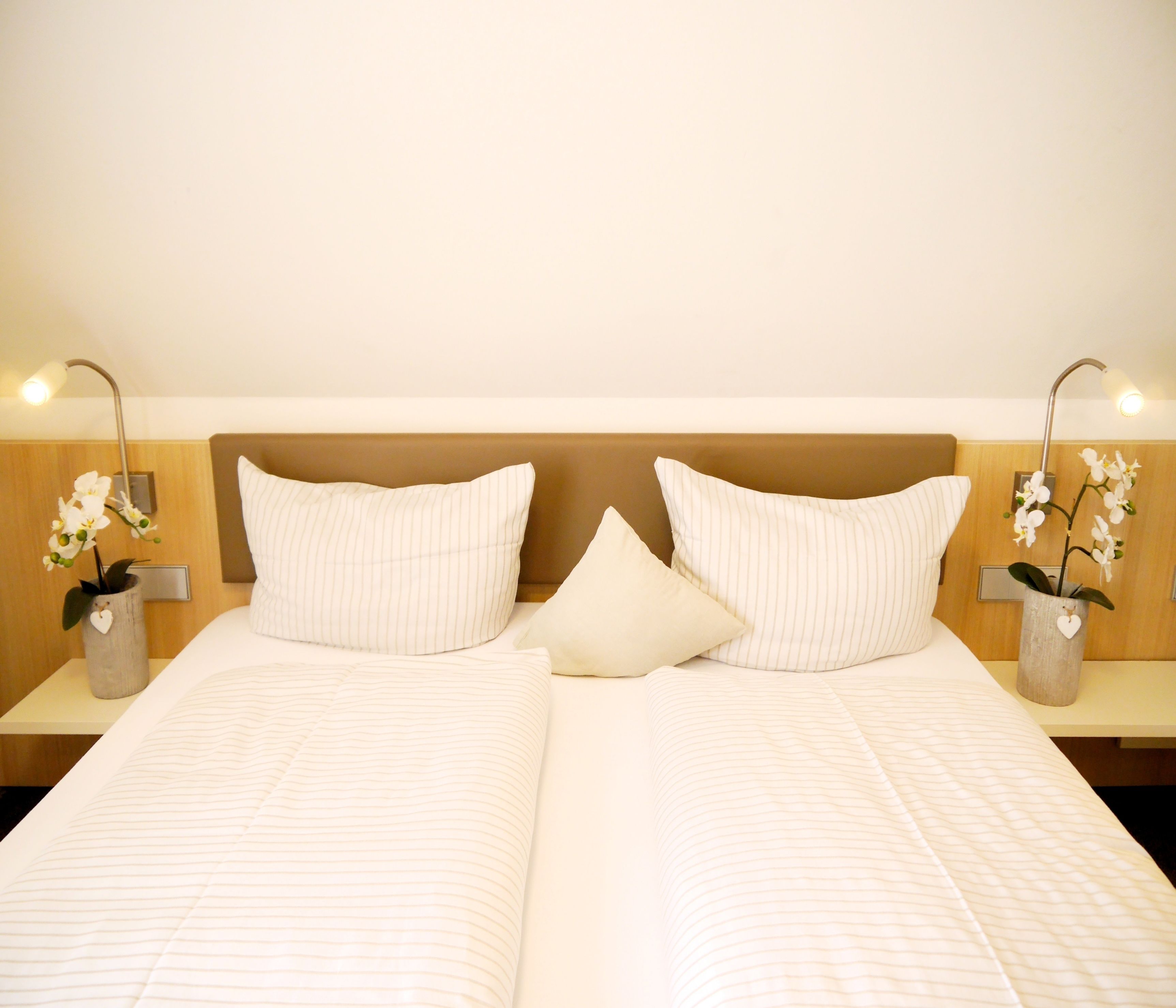 A double bed with two pillows, a wooden headboard, and two bedside tables with lamps and orchid vases.
