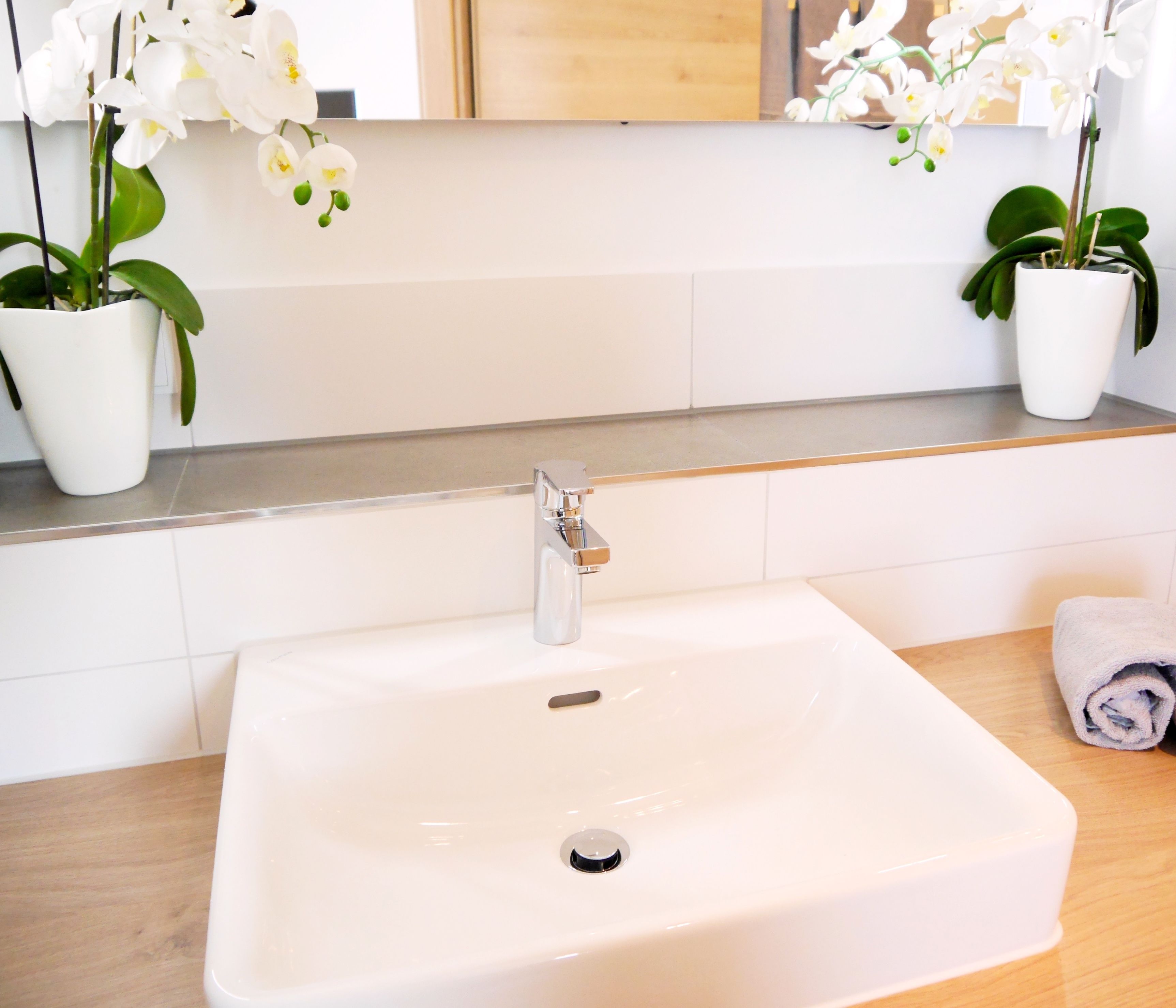 A bathroom with a white sink, a mirror, and two potted orchids.